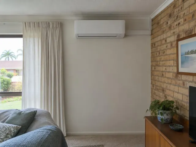 Wall-mounted split system above a plain living room wall beside curtains and a brick feature wall in Mermaid Waters